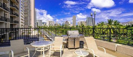 Una terraza en la azotea con mobiliario exterior, una parrilla y vistas al horizonte de la ciudad.