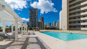 Zona de piscina con tumbonas y vistas a edificios altos al fondo.