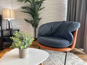 A modern living room with a dark blue armchair, a round white table, a potted plant, a lamp, and a large green plant. - Diamondhead / Ocean View Waikiki Condo on 38th Fl (Honolulu)