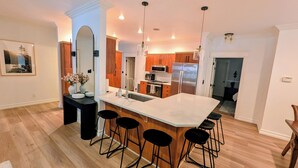 Una cocina moderna con una isla grande, taburetes de bar, armarios de madera y electrodomésticos de acero inoxidable.