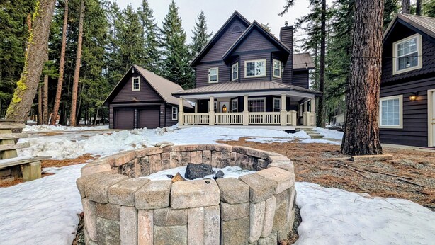 Una casa de dos pisos con un hogar de piedra al frente, rodeada de nieve y pinos.