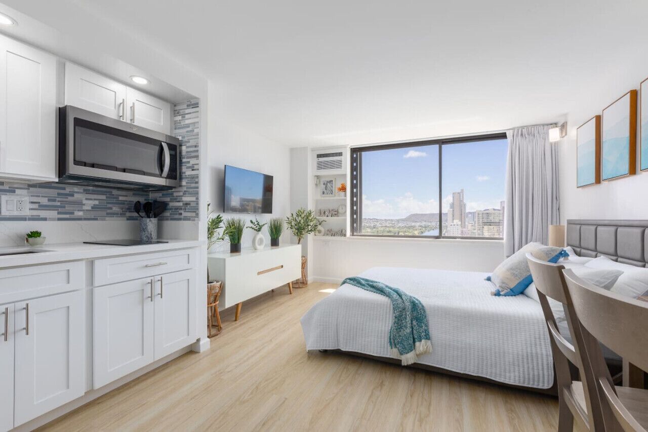 Quarto de hotel moderno com cozinha, uma cama grande, escrivaninha e vista para a cidade.