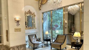 A lobby with two armchairs, a chandelier, and a large mirror.