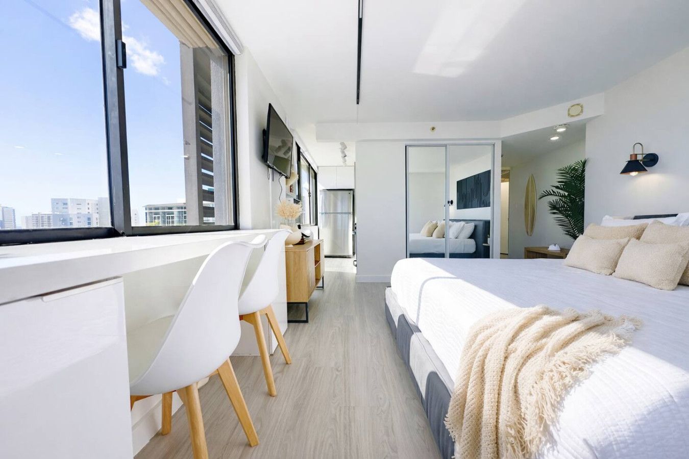 Una habitación de hotel moderna con una cama grande, un escritorio con silla, un televisor y vistas a la ciudad.