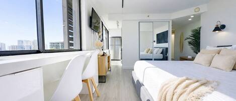 Una habitación de hotel moderna con una cama grande, un escritorio con silla, un televisor y vistas a la ciudad.