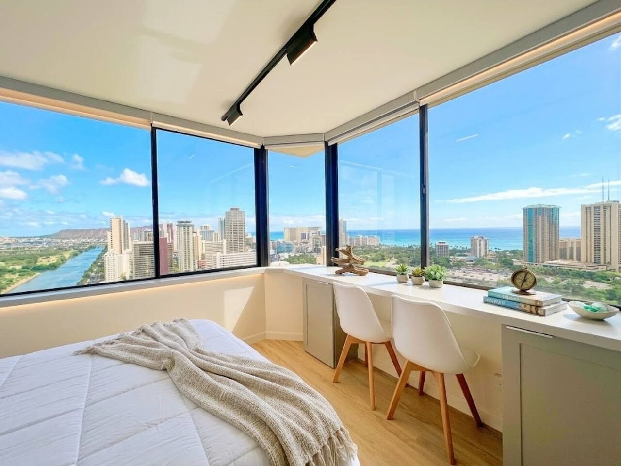 Un dormitorio con un ventanal grande, una cama, un escritorio y vistas a un paisaje urbano.