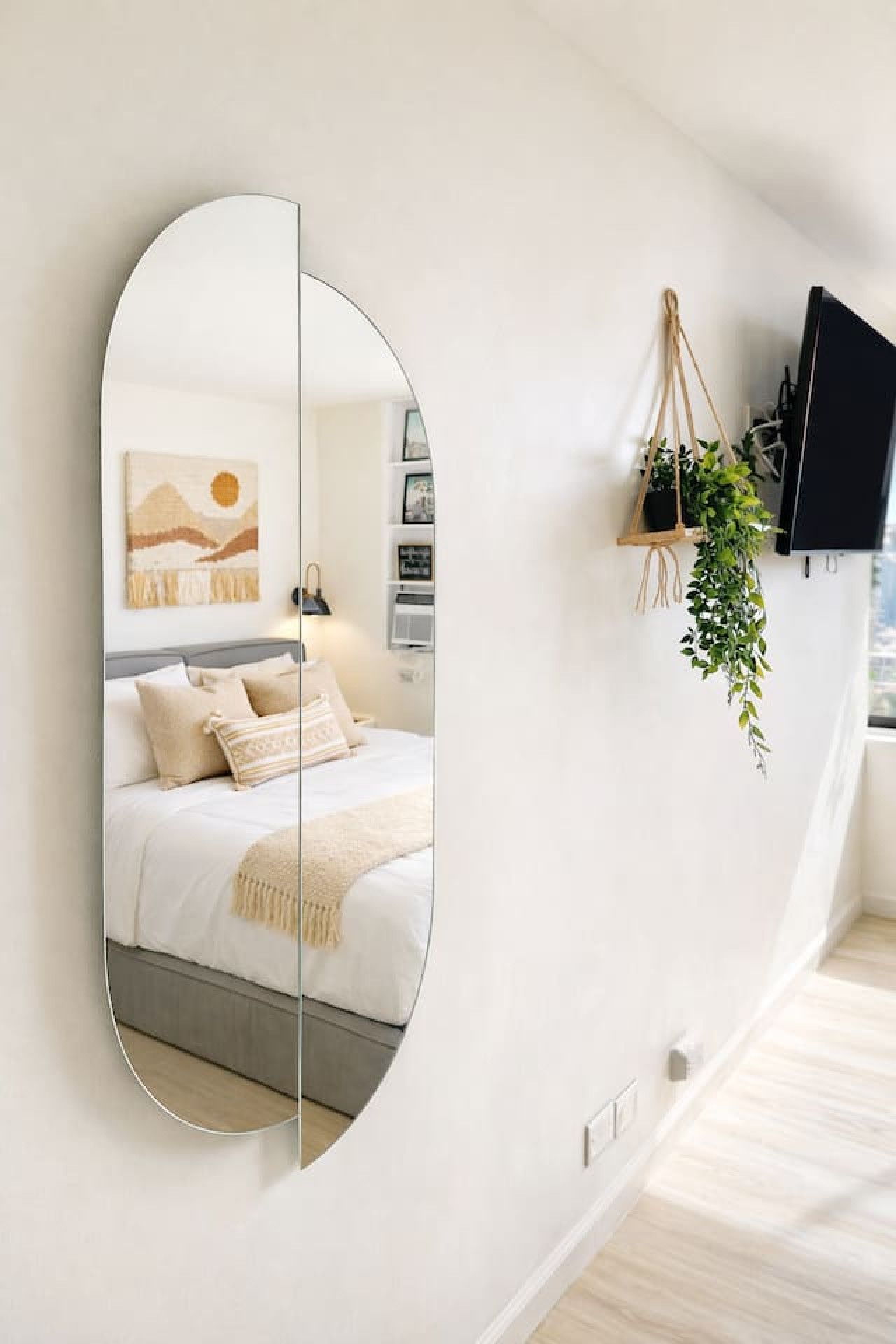 A bedroom with a bed, a large mirror, a wall-mounted TV, and a hanging plant.