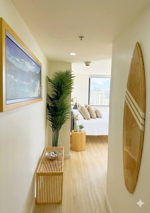 Ein Flur, der in ein Schlafzimmer mit Bett, Pflanze, Holzbank, Surfbrett und einem gerahmten Bild führt.