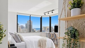 Une chambre moderne avec vue sur la ville, un lit recouvert d’une couette blanche, un bureau et des chaises.