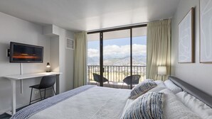Ett hotellrum med en stor säng, ett skrivbord med en stol, en TV och en balkong med stolar.