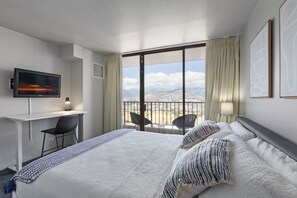 Ein Hotelzimmer mit einem großen Bett, einem Schreibtisch mit Stuhl, einem Fernseher und einem Balkon mit Sitzgelegenheiten.