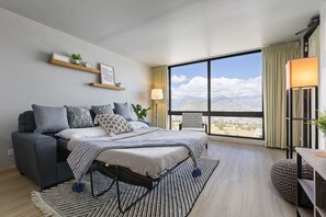 Ein modernes Schlafzimmer mit Bett, Sofa, Schreibtisch und großem Fenster mit Blick auf die Stadt.