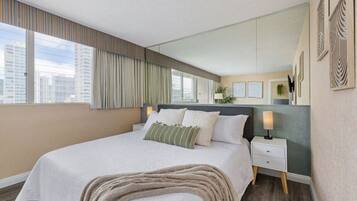 A modern hotel room with a large bed, a nightstand, a mirror, and a view of the city.