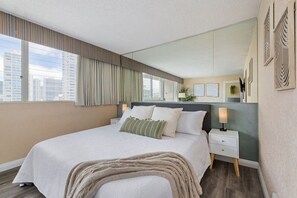 Ett modernt hotellrum med en stor säng, ett nattduksbord, en spegel och utsikt över staden.