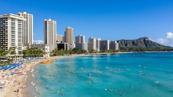 A beach with clear turquoise water, a city skyline, and a mountain in the background.