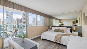 A modern hotel room with a large bed, bedside tables, a desk, and a balcony with a view of the city skyline.