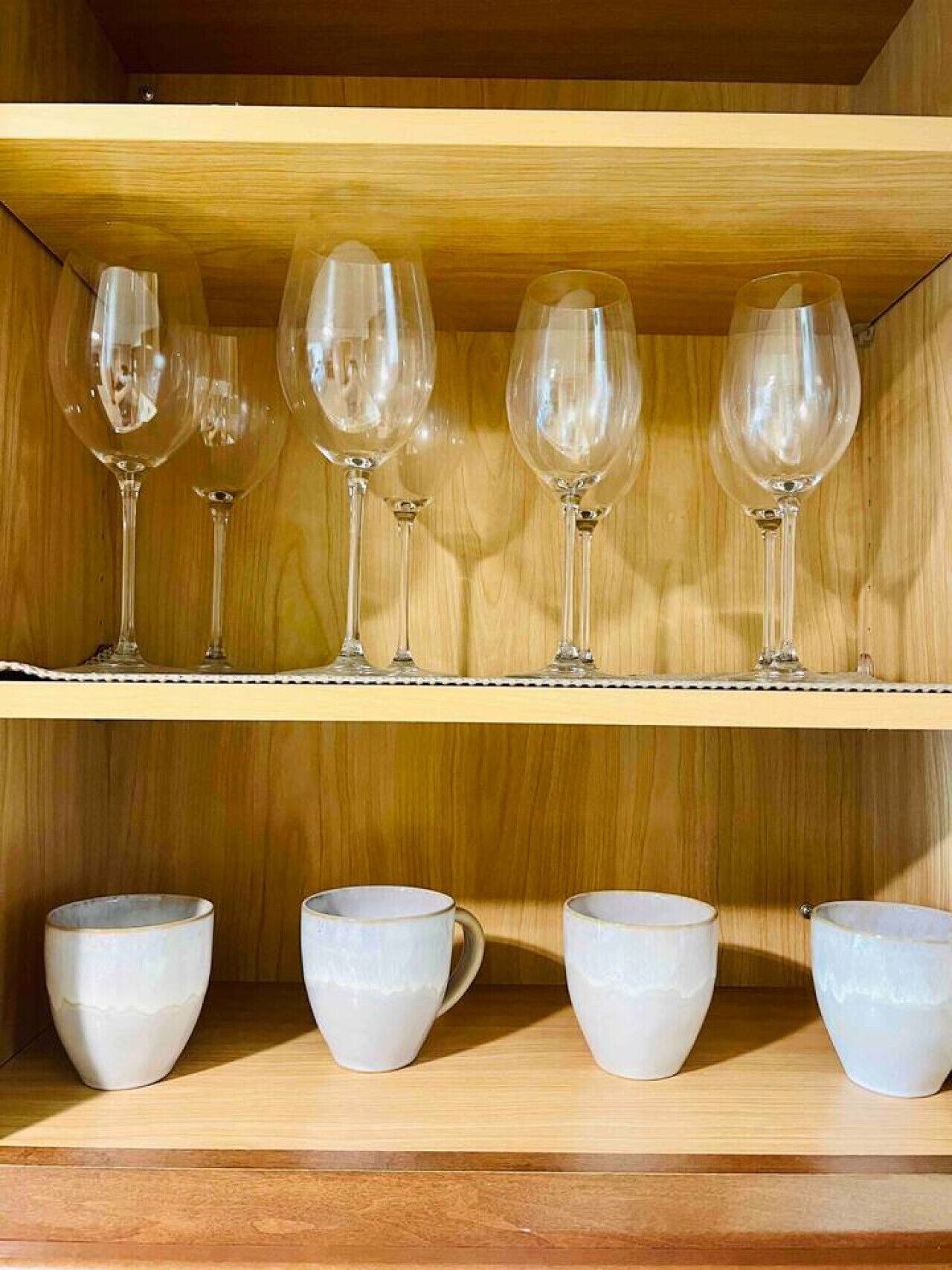 Une étagère en bois avec des verres à vin et des tasses en céramique.