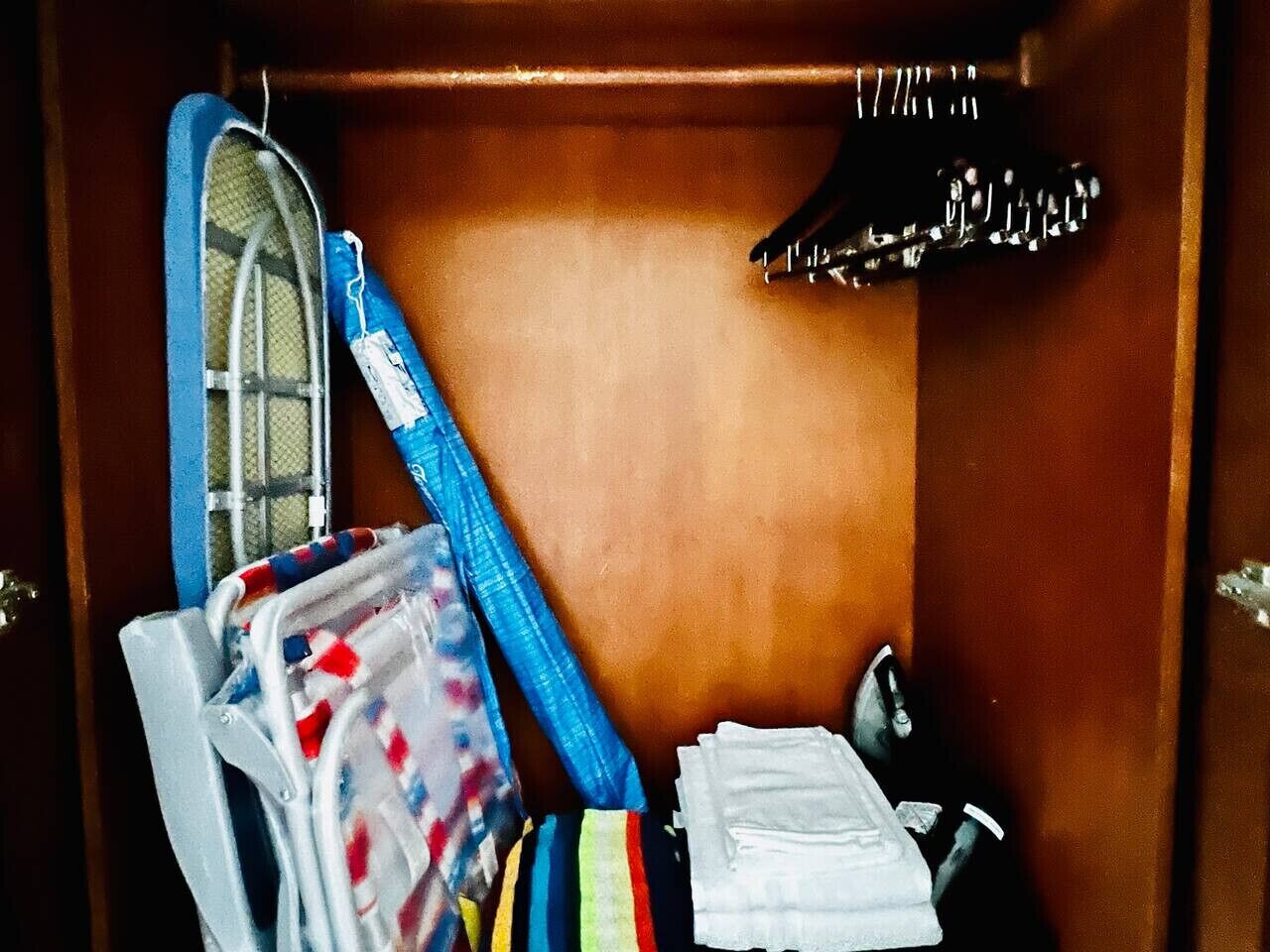 A wooden closet with a hanging shoe rack, a blue and white striped bag, and a white plastic bag.