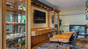 Een moderne eetruimte met een grote houten tafel, zwarte stoelen en een glazen vitrine gevuld met decoratieve objecten.