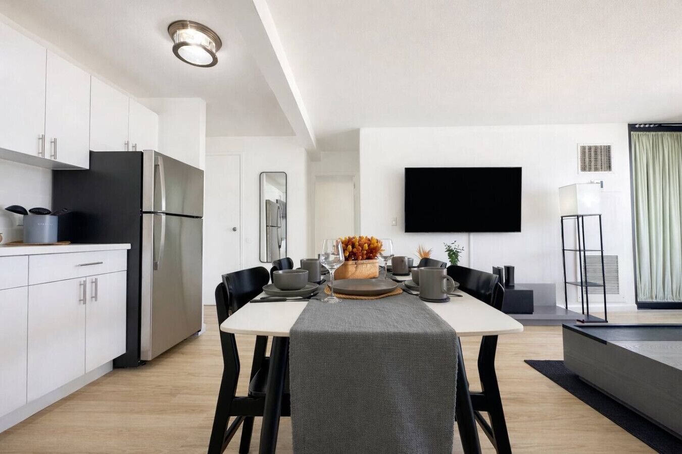 A modern kitchen with white cabinets, a black refrigerator, and a dining area with a table set for four.