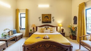 Een hotelkamer met een groot bed, een bank, een houten bijzettafeltje, een nachtkastje, een lamp en een raam met gordijnen.