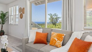 A living room with a sofa, a potted plant, and a view of the ocean through large windows. - Makaha Valley - Few Mins away to Beach (Waianae)
