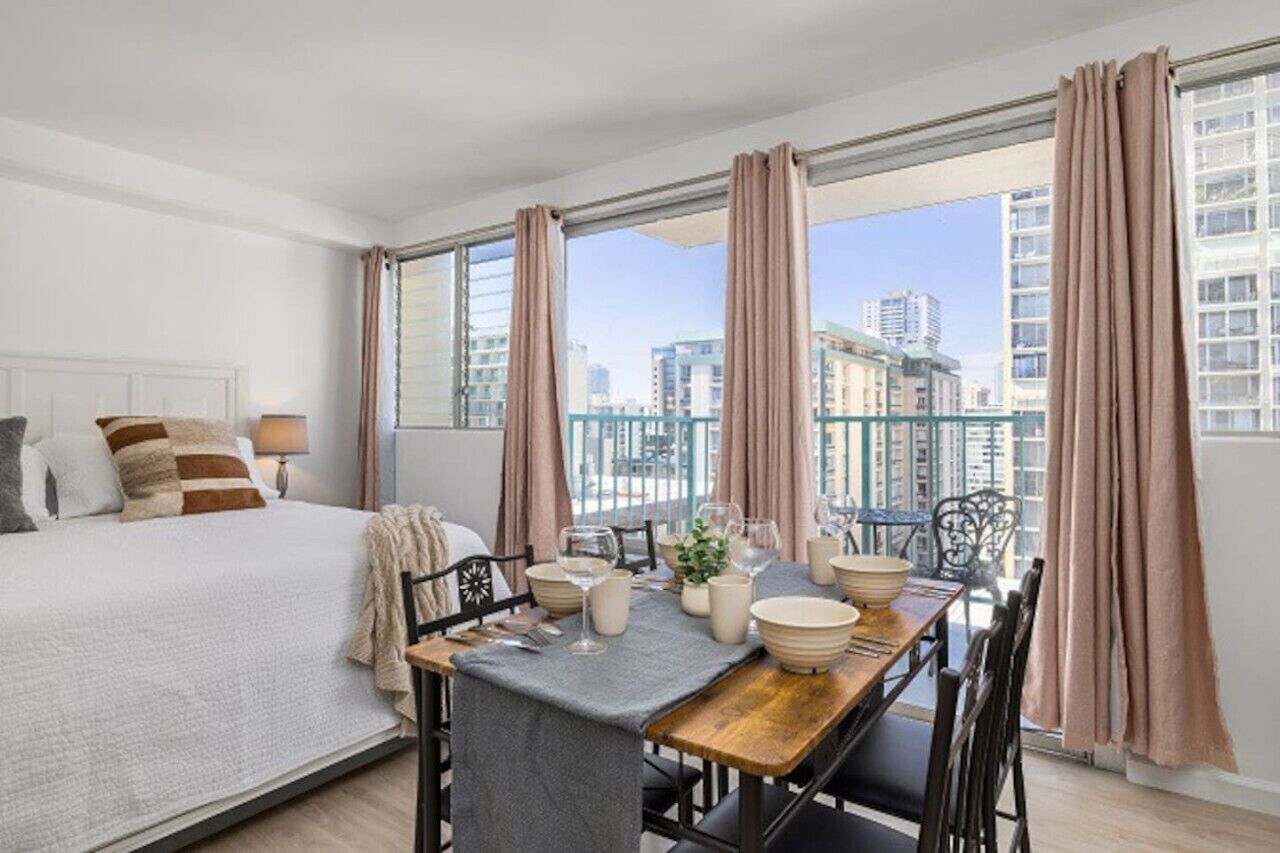 Un dormitorio con una cama grande, una mesa de comedor para dos personas y un balcón con cortinas.