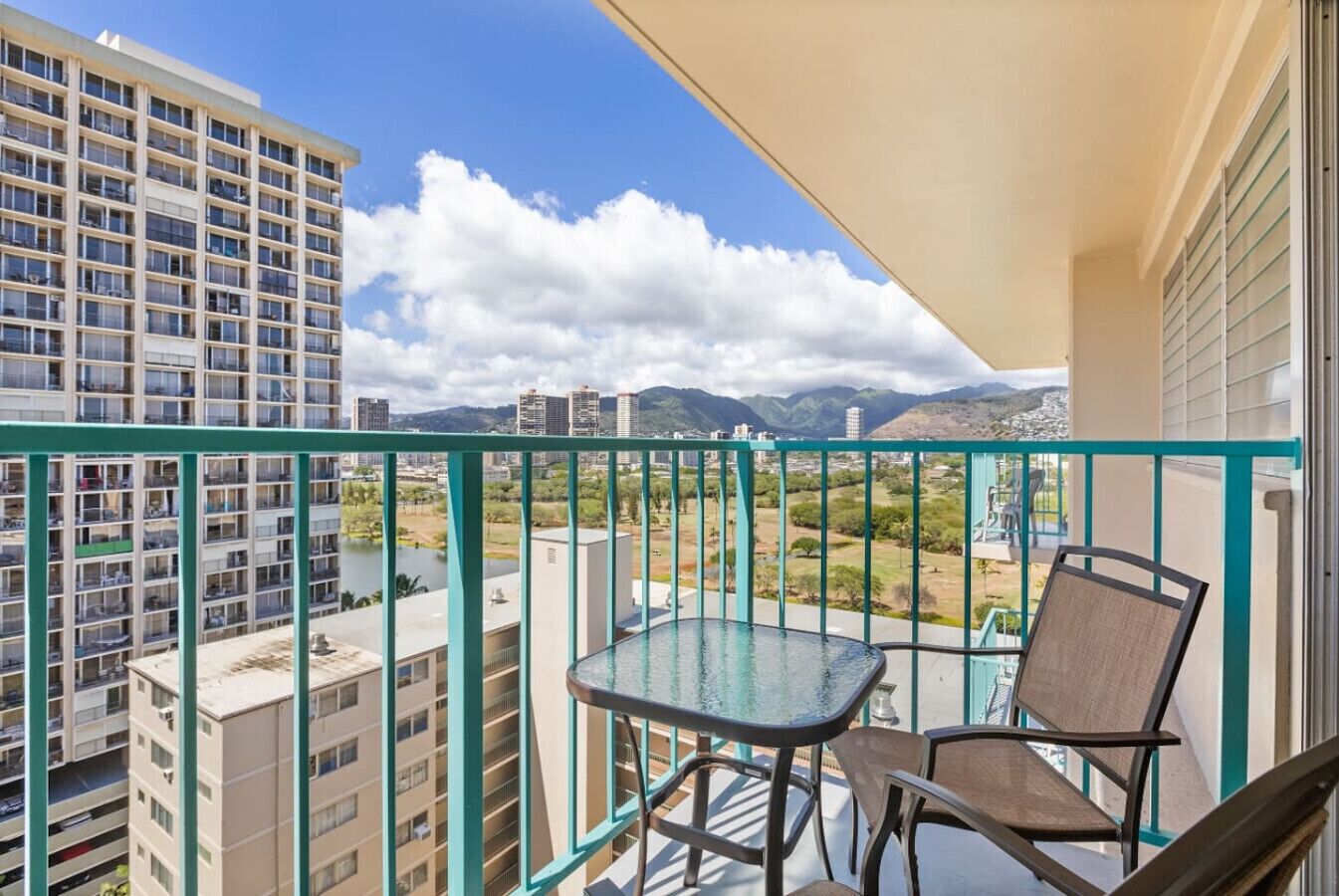 A balcony with a table and chairs, overlooking a cityscape and mountains.