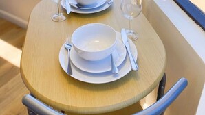 A dining table set with white plates, bowls, and cutlery, positioned near a window with a view of a river and buildings. - HM15 Rare Find - Corner Ocean View Studio at Waikiki (Honolulu)