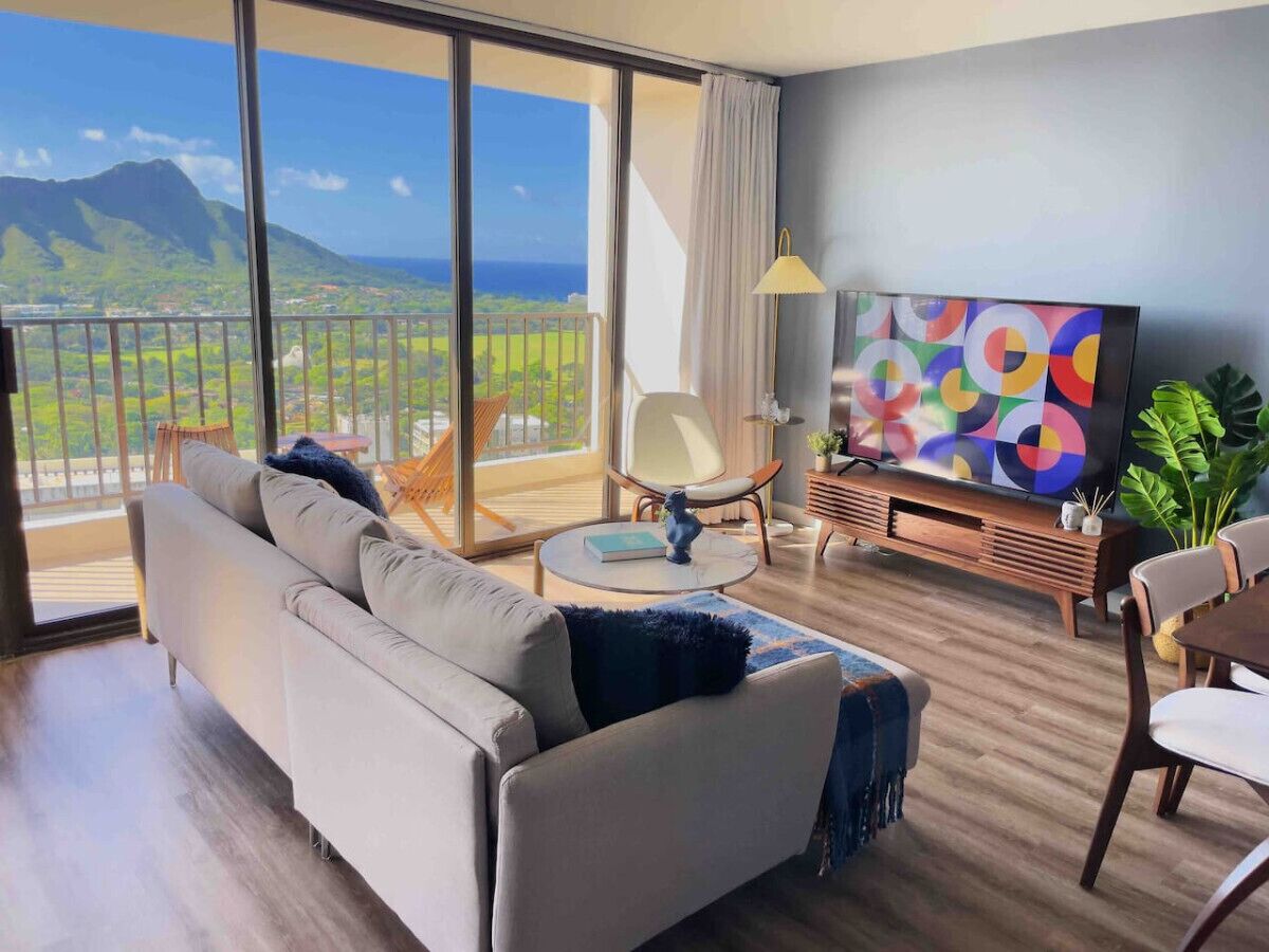 Un salon moderne avec un canapé, une table basse et un téléviseur. Il y a un balcon qui offre une vue sur le paysage.