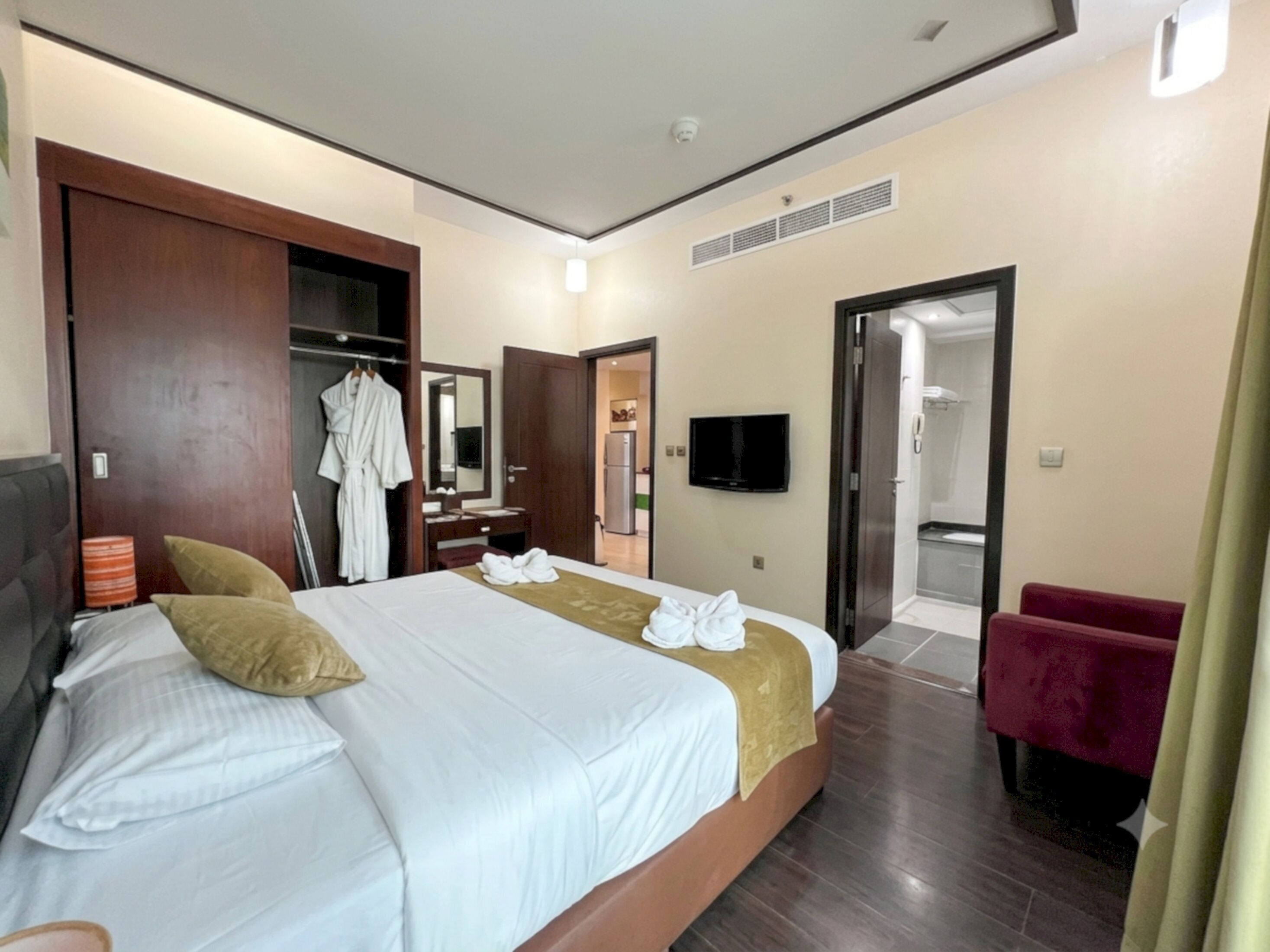 A hotel room with a large bed, a wardrobe, a mirror, a television, and a bathroom visible through an open door.
