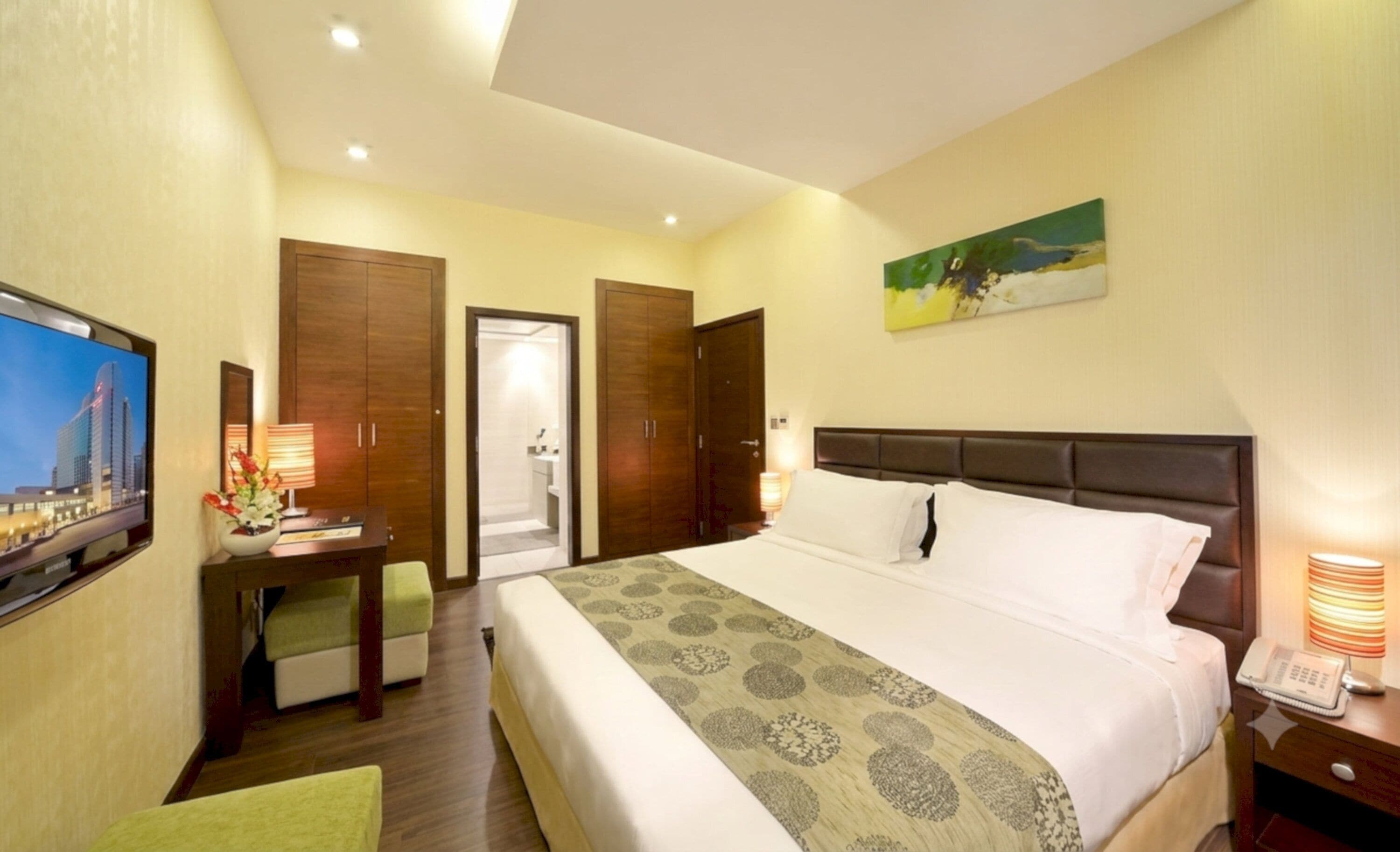 A hotel room with a bed, a desk with a lamp, a television, and a painting on the wall.