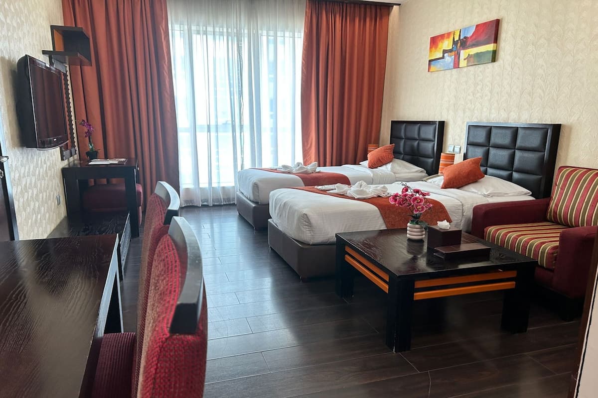 Ein Hotelzimmer mit zwei Betten, einem Sofa, einem Fernseher und einem Tisch mit Blumenvase.