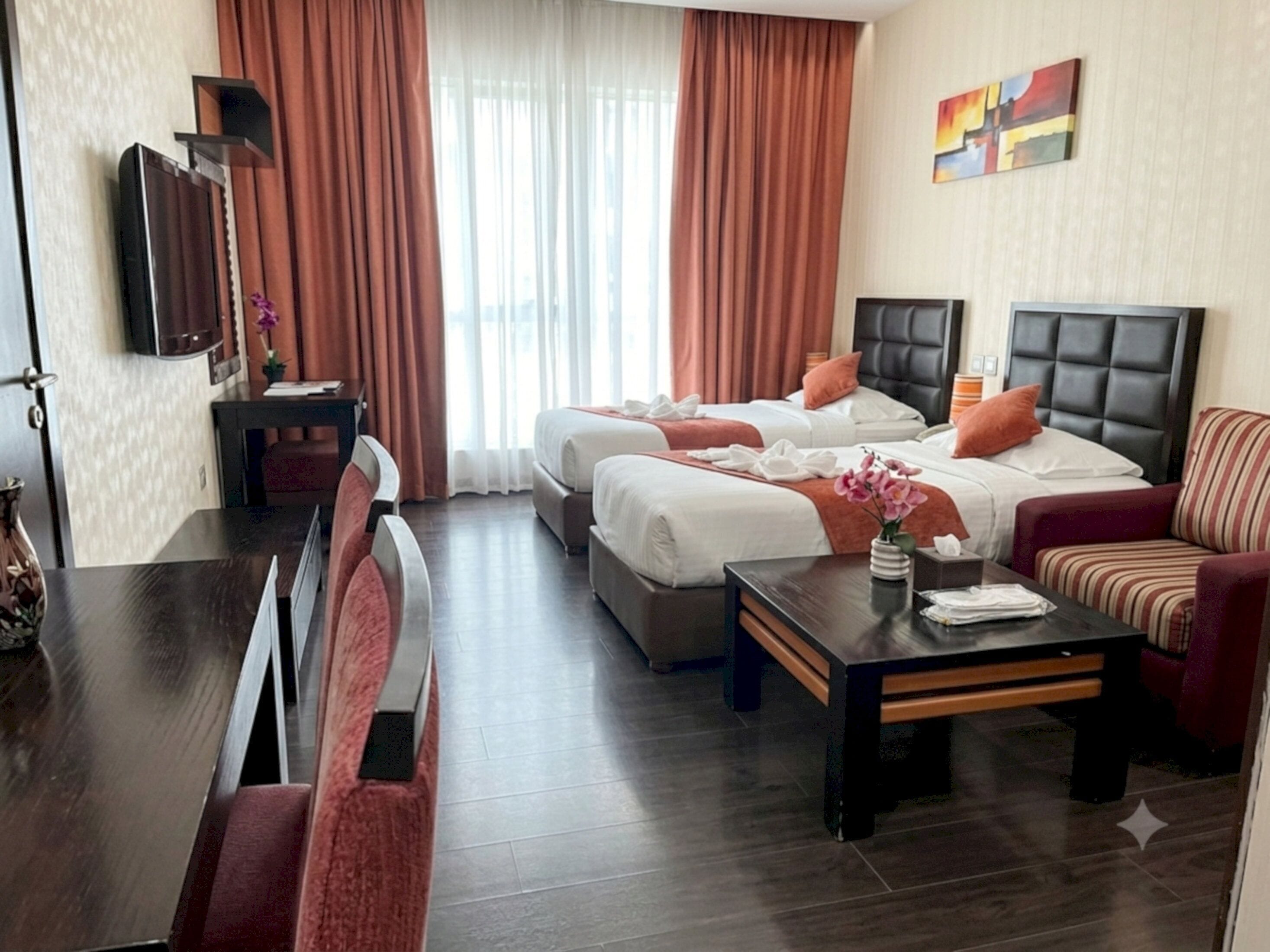 Habitación de hotel con dos camas, un sofá, una mesa de comedor y una televisión.