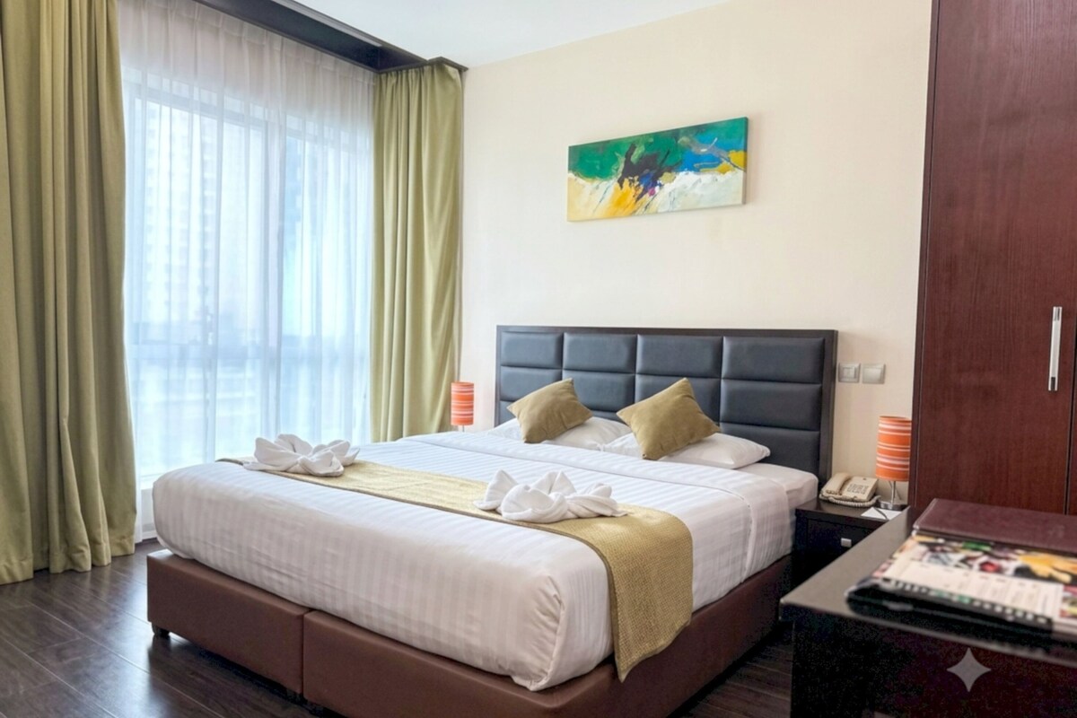 Een hotelkamer met een groot bed, een hoofdbord, een schilderij aan de muur, een bureau met een lamp en een kledingkast.