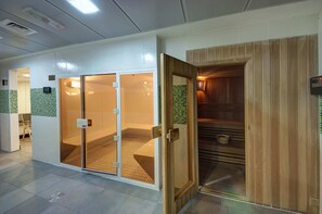 Een moderne hotel lobby met een sauna, een douchecabine met glazen wanden en een houten sauna-ingang.