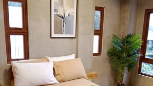 Une chambre à coucher avec un lit, un tableau abstrait encadré, une plante en pot et deux fenêtres.