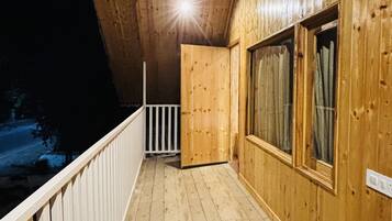 Un balcón de madera con barandilla, una puerta de madera y ventanas.