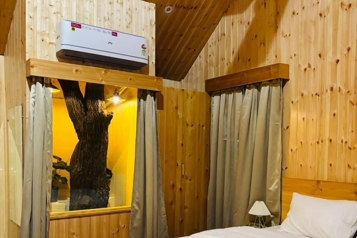 A wooden cabin room with a bed, a large tree trunk, and a ceiling fan.