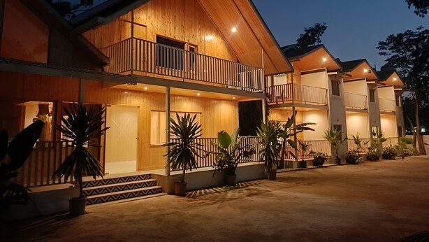 A multi-story wooden building with balconies, potted plants, and a concrete ground. - Bundela Woods Cottage and Restaurant (Rajnagar)
