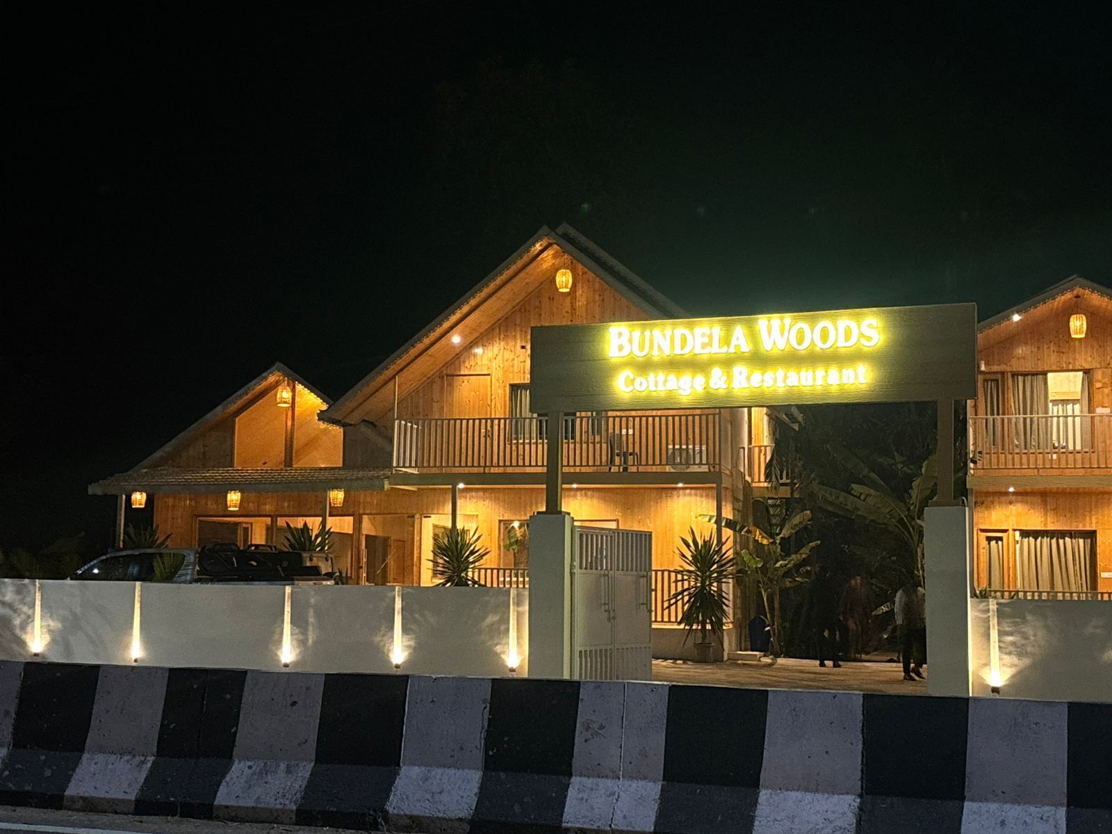A two-story wooden building with a sign reading "Bundela Woods Cottage & Restaurant."