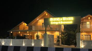A two-story wooden building with a sign reading "Bundela Woods Cottage & Restaurant."
