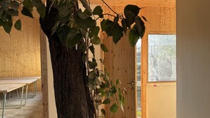 A room with a large tree trunk centerpiece, wooden walls, a patterned floor, and a door leading outside. - Bundela Woods Cottage and Restaurant (Rajnagar)