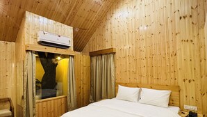 A wooden-paneled room with a bed, a chair, and an air conditioning unit mounted on the wall. - Bundela Woods Cottage and Restaurant (Rajnagar)