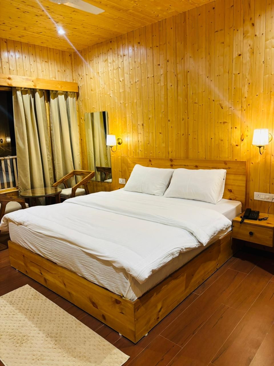 Een slaapkamer met houten lambrisering, een groot bed, nachtkastjes en een spiegel.