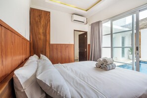 A hotel room with a wooden headboard, a large bed with white linens, a view of a swimming pool, and a sliding glass door to the outdoors. - Bhiseka Villa Jimbaran by Aishwarya Bali (Jimbaran)