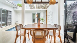 Un coin repas avec une table et des chaises en bois, un vase rempli de fleurs et un luminaire suspendu.