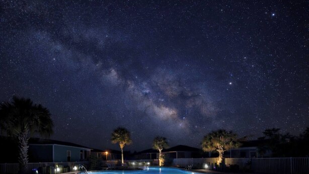 Et poolområde om natten med en stjerneklar himmel og Mælkevejen.