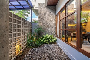A modern outdoor area with a stone wall, a wooden fence, and a gravel path leading to a dining area. - Villa Queeno - Nusa Dua (Nusa Dua)