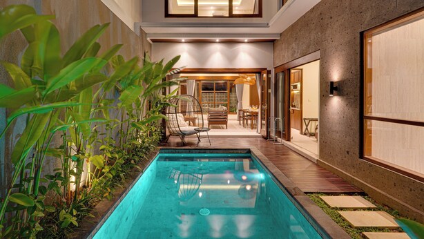 Un espace piscine extérieur moderne, doté d’une terrasse en bois, de chaises longues et d’un espace repas fermé par des parois de verre.